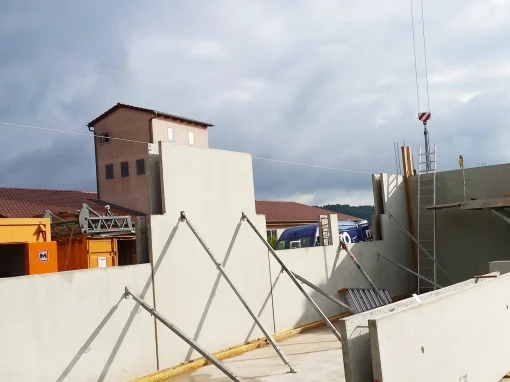 20160729_081034_web-webp Mehrere Betonfertigteile werden auf einer Baustelle mit Stützen fixiert. Im Hintergrund stehen orange Baucontainer, ein Kranhaken und ein Gebäude mit rotem Dach