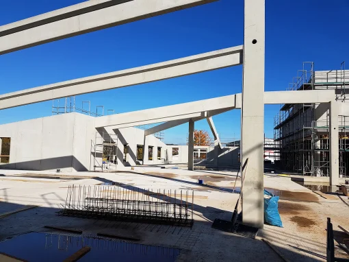20161031_123433_web-webp Auf einer sonnigen Baustelle stehen große Betonträger und Wände eines Neubaus. Im Vordergrund liegen Baustahlmatten und Pfützen auf dem Boden