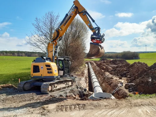 Abwasseranlage-Duerrnbuch_1-webp Gelber Kettenbagger neben einem Graben mit verlegten Rohren auf einer weitläufigen Baustelle in grüner Landschaft bei sonnigem Wetter