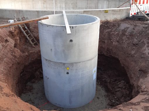 Abwasserbeseitigung-–-Markt-Taschendorf_4 Großer runder Betonschacht in einer Baugrube auf einer Baustelle mit umliegenden Absperrungen und Baggern im Hintergrund bei herbstlichem Wetter