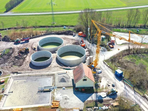 Klaeranlage-Sugenheim_2jpg-webp Luftaufnahme einer im Bau befindlichen Kläranlage mit drei runden Betonbecken, Baufahrzeugen, einem gelben Kran und umliegender Wiese in ländlicher Umgebung