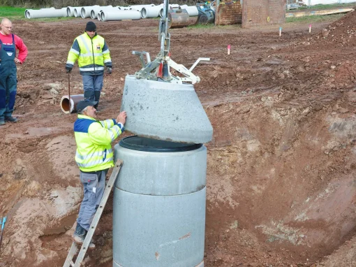 Tiefbau_Erschliessung_Baugrund_Heilsbronn_4-webp-2 Ein Arbeiter auf einer Leiter führt die Montage eines Schachtdeckels durch. Der Betondeckel wird per Kran abgesenkt. Drei Kollegen beobachten das Geschehen