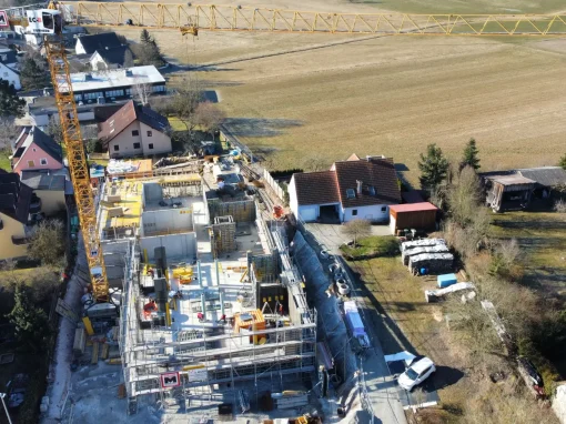 3_Grundschule Schalkhausen Luftaufnahme einer Baustelle in einem Wohngebiet mit einem großen gelben Kran. Mehrstöckiges Gebäude im Rohbau mit Baustellenmaterial und umgeben von Einfamilienhäusern