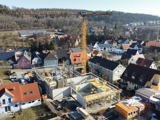 4_Grundschule Schalkhausen (Titelbild) Luftaufnahme einer Baustelle in einem Wohngebiet mit einem gelben Turmdrehkran, mehreren Baucontainern und Rohbau, umgeben von Einfamilienhäusern und Bäumen