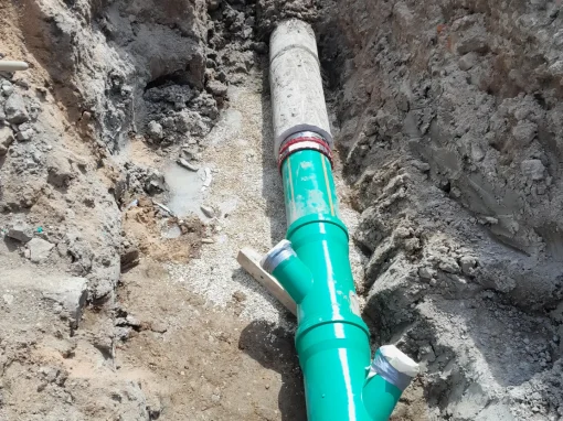 4_Kanalsanierung Hofgarten Ansabch Grüne Kunststoff-Abwasserleitung mit mehreren Abzweigen wird in einem offenen Graben verlegt, verbunden mit grauen Betonrohren und metallischen Schellen