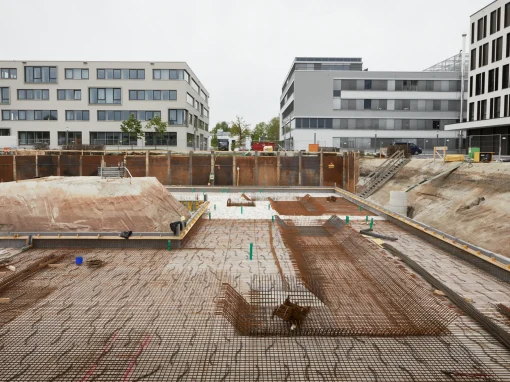 4_Tucher Campus Marienberg BA4 Baustelle mit vorbereiteten Stahlbewehrungen für den Betonboden. Im Hintergrund moderne Bürogebäude und Spundwände, ein Erdhügel liegt im Baugrubenbereich