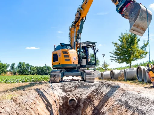 4_Umbau Kläranlage Simmershofen (Titelbild) Ein Arbeiter überprüft ein verlegtes Betonrohr in einem tiefen Graben, während ein Bagger darüber steht, daneben liegen weitere Rohre bereit