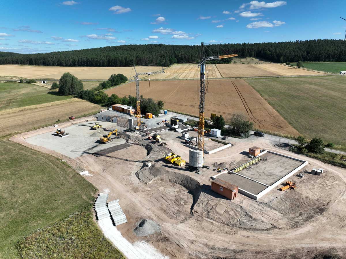 Großes Industriegebäude im Bau mit umfassendem Gerüst an der Seite unter blauem Himmel auf einem weiträumigen Baustellengelände mit Bauschutt und Maschinen